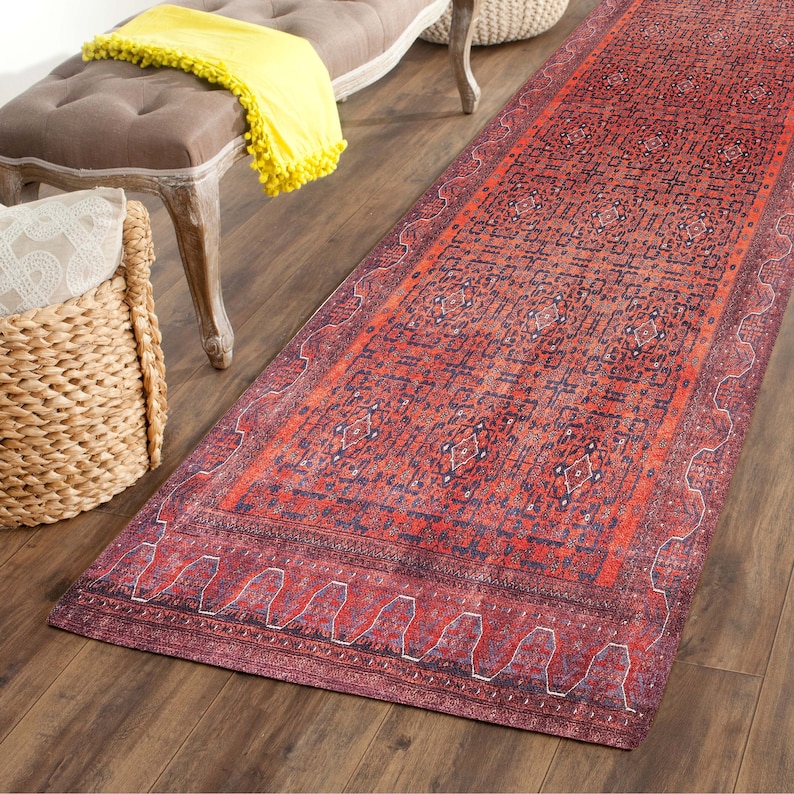 May include: A red and blue patterned runner rug with a distressed look. The rug has a geometric design with a border of repeating shapes.