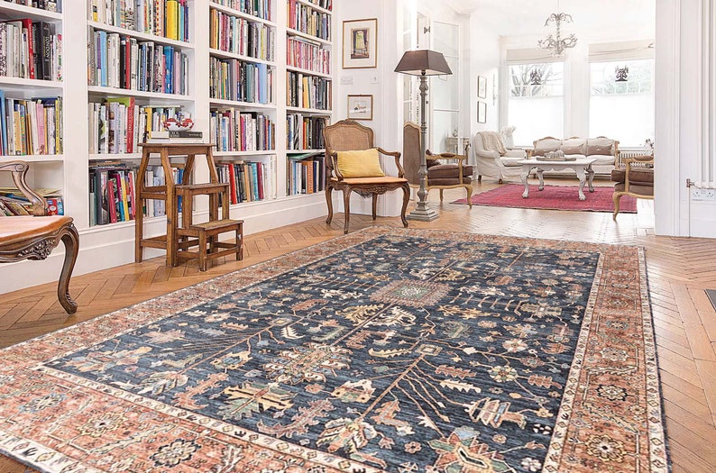 K&ouml;nnte beinhalten: Ein dunkelblauer Teppich mit traditionellem persischem Design. Der Teppich hat einen roten und cremefarbenen Rand und liegt auf einem Holzboden in einem Raum mit wei&szlig;en W&auml;nden und B&uuml;cherregalen.