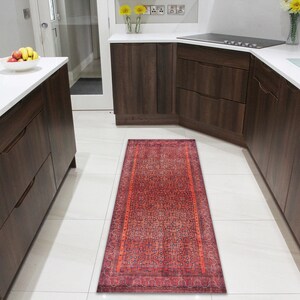 May include: A red and blue patterned runner rug with a geometric design. The rug is placed in a kitchen with white tile floors and brown cabinets.