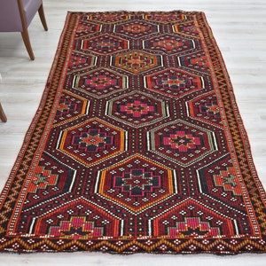 Pu&ograve; includere: Un tappeto da corridoio rosso, arancione, nero e verde con un motivo geometrico. Il tappeto ha un bordo con frange.