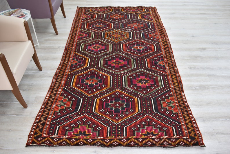 Pu&ograve; includere: Un tappeto da corridoio rosso, arancione, nero e verde con un motivo geometrico. Il tappeto ha un bordo con frange.