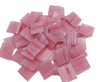 May include: A pile of pink glass mosaic tiles with a striated pattern. The tiles are square and have a translucent appearance.