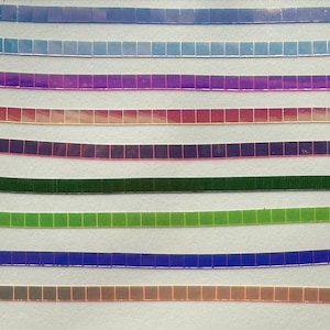 Könnte beinhalten: Draufsicht auf acht Farbstreifen. Jeder Streifen besteht aus kleinen, quadratischen Kacheln. Die Farben reichen von Blau über Lila, Grün bis hin zu Kupfer. Die Streifen sind leicht gebogen und horizontal angeordnet.