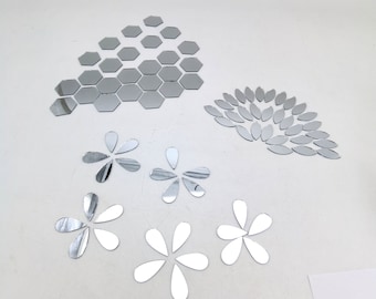 May include: A collection of silver mirror wall decals including a cluster of small hexagons, a fan-shaped arrangement of leaf-shaped pieces, and four individual flower-shaped designs composed of five teardrop-shaped mirror petals each.