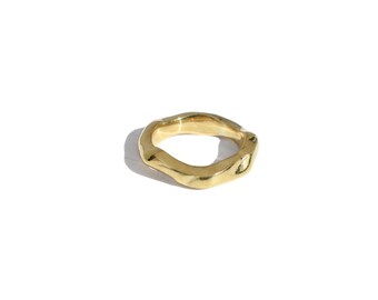 May include: A gold-colored ring with an organic, irregular shape. The ring appears to be made of metal and has a smooth, polished finish. The design is modern and minimalist, suitable for everyday wear. The ring is shown on a white background.