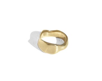 Puede incluir: Un anillo dorado con una forma irregular y orgánica. El anillo tiene una superficie lisa y pulida y una banda ancha. El diseño es moderno y minimalista, adecuado para el uso diario. El anillo se muestra sobre un fondo blanco.