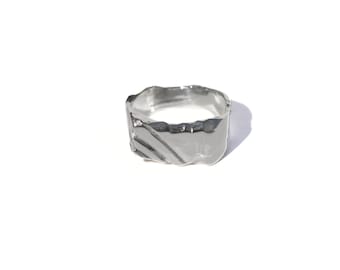 May include: A silver ring with a textured, wavy design. The ring is thick and has a wide band.