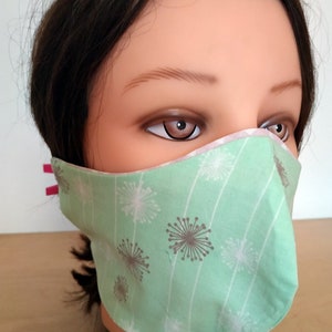 May include: A green face mask with a white and gray dandelion pattern. The mask has pink elastic ear loops.