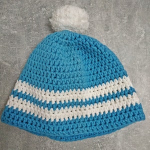 Puede incluir: Un gorro azul de ganchillo con rayas blancas y un pompón blanco en la parte superior.