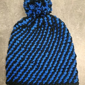 Puede incluir: Gorro de punto azul y negro con un pompón esponjoso en la parte superior.