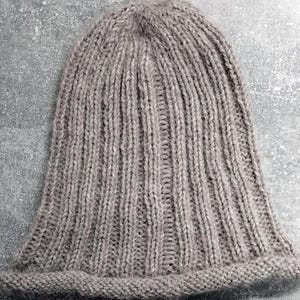 Puede incluir: Un gorro de punto gris con textura de canalé. El gorro está hecho de un material suave y cálido y tiene un diseño simple y clásico.