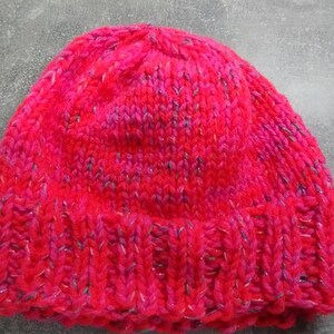 Puede incluir: Un gorro de punto rosa y morado con un hilo brillante tejido en todo.