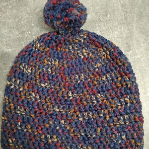 Puede incluir: Un gorro de punto azul, marrón y rojo con un pompón esponjoso en la parte superior.