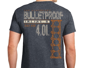 May include: Dark gray t-shirt with the text "THE LEGENDARY BULLETPROOF INLINE 6 242 CID 4.0L" in white and orange. A stylized orange engine block graphic is on the right side of the shirt. The shirt is made of a soft material.