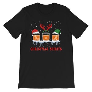 May include: Black t-shirt with a Christmas-themed design featuring three glasses of whiskey with Santa hats and reindeer antlers. The text "Christmas Spirits" is printed below the glasses.
