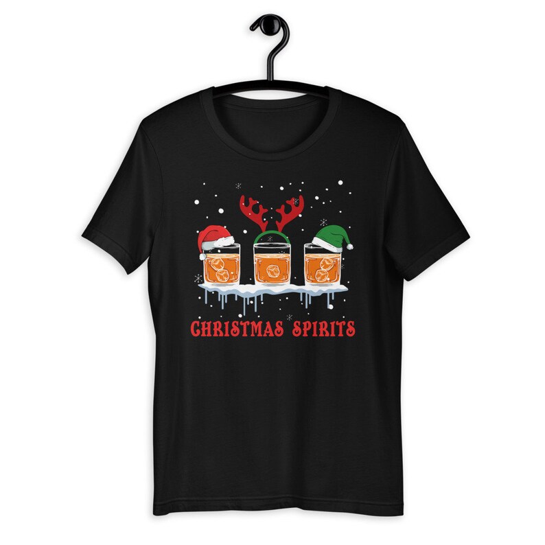 May include: Black t-shirt with a Christmas-themed design featuring three glasses of whiskey with Santa hats, reindeer antlers, and elf hats. The text "Christmas Spirits" is printed below the glasses.
