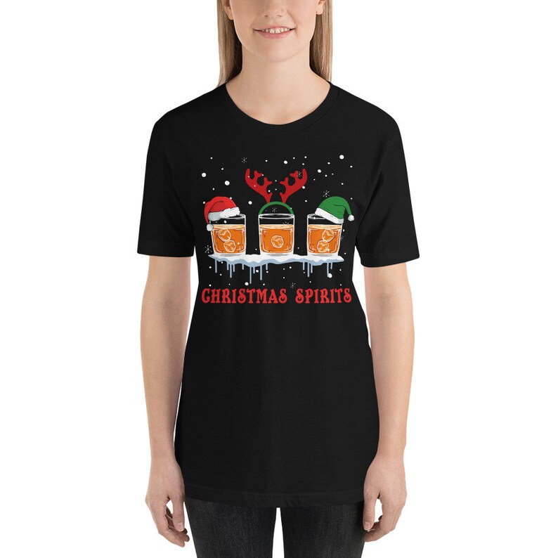 May include: Black t-shirt with a Christmas-themed design featuring three glasses of orange liquid with Santa hats and reindeer antlers. The text "Christmas Spirits" is printed below the glasses.