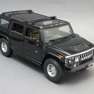 Può includere: Un modello di auto Hummer H2 nero con ruote argentate e interni dettagliati. Il modello presenta un portapacchi, una protezione del paraurti anteriore e una presa d'aria sul cofano. Il veicolo è una replica in miniatura del SUV full-size.