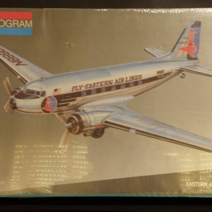 Op de afbeelding: Een modelbouwpakket van een zilveren en blauwe Eastern Airlines DC-3 vliegtuig met de tekst "Fly-Eastern Air Lines" aan de zijkant. De kit is van Monogram en is een 1/48 schaalmodel.
