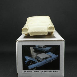 Könnte beinhalten: Eine cremefarbene Modellkarosserie sitzt auf einer Box mit einem blauen Auto mit geöffneter Motorhaube. Die Box ist mit "58 New Yorker Conversion Pack" beschriftet. Das Modellauto ist ein Oldtimer.