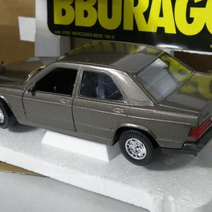 May include: A gray 1/18 scale diecast model car of a Mercedes-Benz 190 E. The car is on a white base and the box says "Bburago" and "Made in Italy".