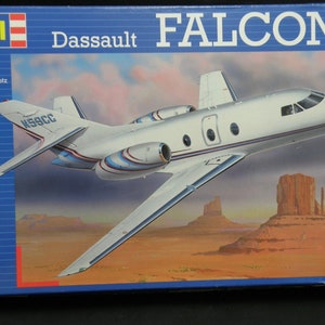 Op de afbeelding: Een modelbouwpakket van een Dassault Falcon 10 privéjet. De doosafbeelding toont een wit en blauw vliegtuig met rode accenten dat over een woestijnlandschap vliegt. De kit is op schaal 1:48 en bevat de tekst "Dassault FALCON 10" en "04217".