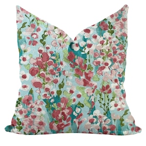 May include: A decorative pillow with a floral pattern. The pillow features a light blue background with a design of pink, red, and white flowers and green leaves. The pillow is square-shaped and has a soft, textured appearance.