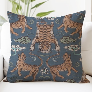 May include: A blue throw pillow with a repeating pattern of orange tigers on a blue background. The tigers are in various poses, including standing, walking, and lying down. The pattern also includes stylized clouds.