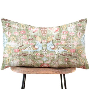 May include: A green, rectangular pillow with a floral and bird pattern. The pillow is sitting on a wooden chair with black metal legs.