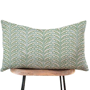 May include: A rectangular decorative pillow with a botanical leaf pattern. The pillow features a light blue background with a repeating pattern of green and white leaves. The pillow is resting on a small wooden stool with black metal legs.