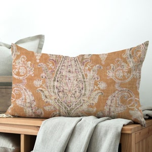 May include: A rectangular throw pillow with a brown background and a white paisley pattern. The pillow is sitting on a wooden shelf with a white throw blanket.