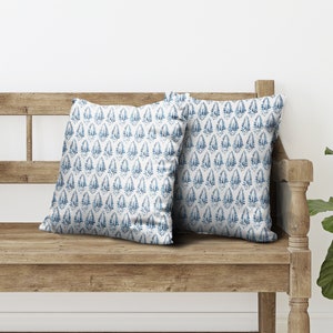 May include: Two blue and white patterned throw cushions on a wooden bench. The cushions have a repeating pattern of blue leaves on a white background.