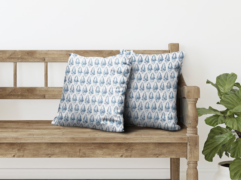 May include: Two blue and white patterned throw cushions on a wooden bench. The cushions have a repeating pattern of blue leaves on a white background.