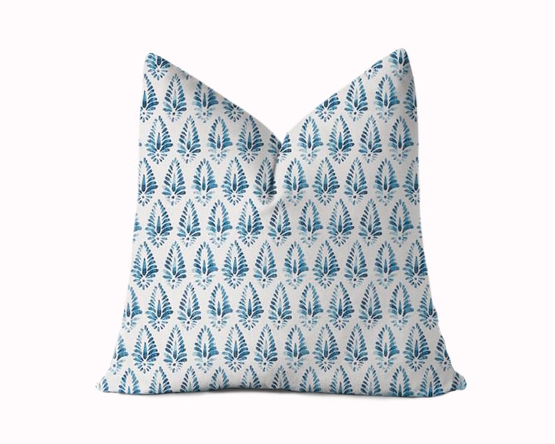 May include: A white throw pillow with a blue and white geometric pattern. The pattern features a repeating design of stylised leaves.