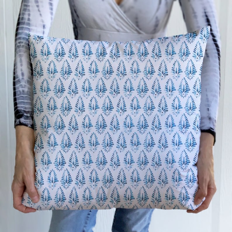 May include: A white cushion with a blue and white geometric pattern. The pattern is a repeating design of stylised teardrop shapes.