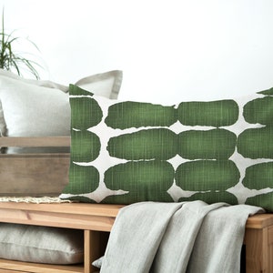 May include: A green and white rectangular throw pillow with an abstract pattern. The pillow is sitting on a wooden surface with a blanket draped over it.