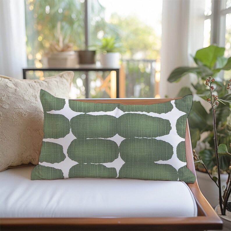 May include: A green and white patterned throw pillow with a geometric design. The pillow is sitting on a white sofa with a wooden frame.