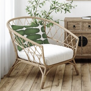 May include: A wicker chair with a white cushion and a green patterned pillow. The chair is sitting on a wooden floor.
