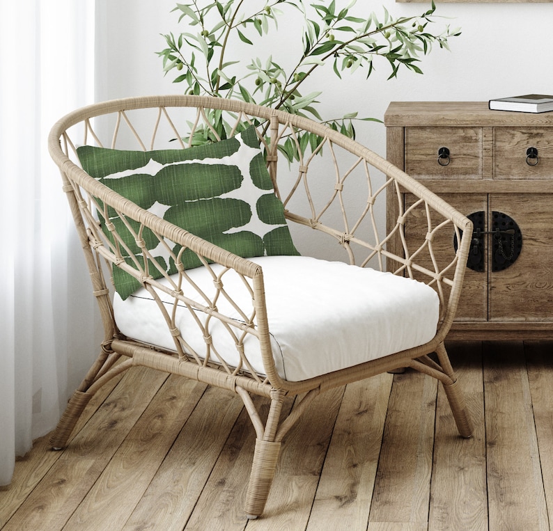 May include: A wicker chair with a white cushion and a green patterned pillow. The chair is sitting on a wooden floor.