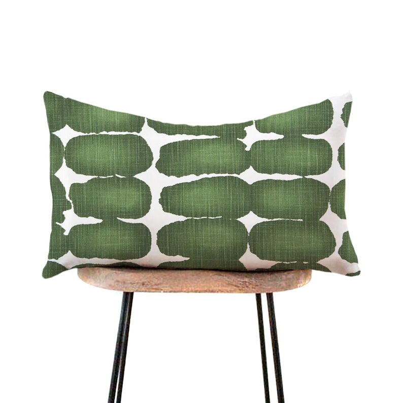May include: A green and white lumbar cushion with an abstract pattern. The cushion is sitting on a wooden chair with black metal legs.