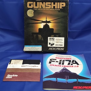 May include: A retro computer game box for "Gunship: The Helicopter Simulation" featuring a helicopter silhouette. Includes a floppy disk labelled "Burroughs" and a game manual for "F-117A Stealth Fighter 2.0".