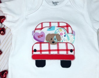 May include: White baby onesie with a red and white checkered truck carrying a dog and hearts. The truck has a purple heart with the text "XOXO" on it.