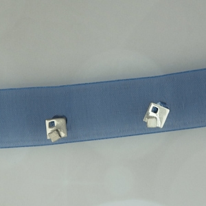 Può includere: Due orecchini d'argento con un design geometrico, esposti su un nastro blu.