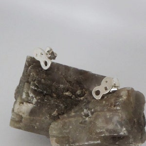 Può includere: Due orecchini d'argento con un design geometrico unico. Gli orecchini sono esposti su una roccia marrone e ruvida.