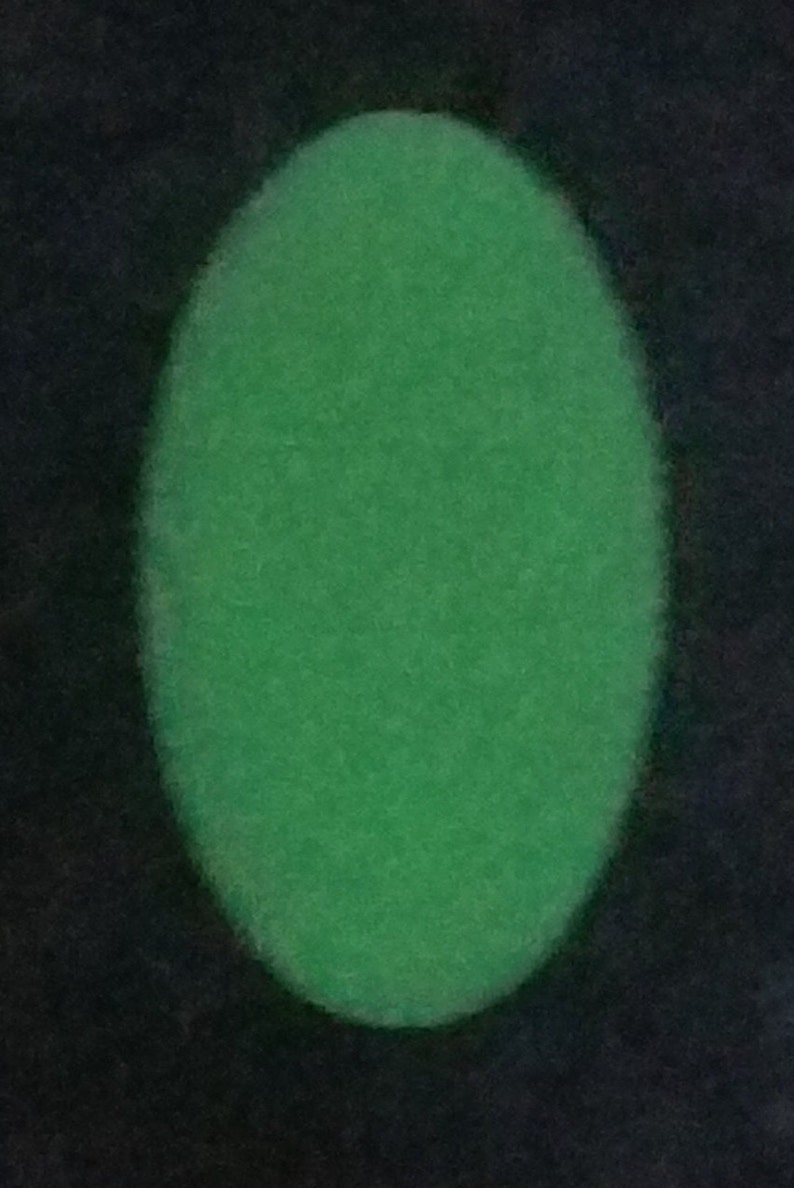 May include: A solid, vibrant green oval shape with a soft, slightly fuzzy texture. The oval is centered against a dark, contrasting background, creating a clear visual distinction between the bright green form and the surrounding dark space.