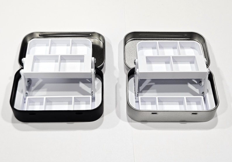 May include: Two metal storage boxes with a white plastic insert. The box on the left is black and the box on the right is silver.