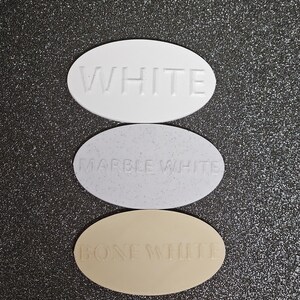May include: Three oval-shaped paint chips, each with a different shade of white. The top chip is labelled "WHITE", the middle chip is labelled "MARBLE WHITE", and the bottom chip is labelled "BONE WHITE".