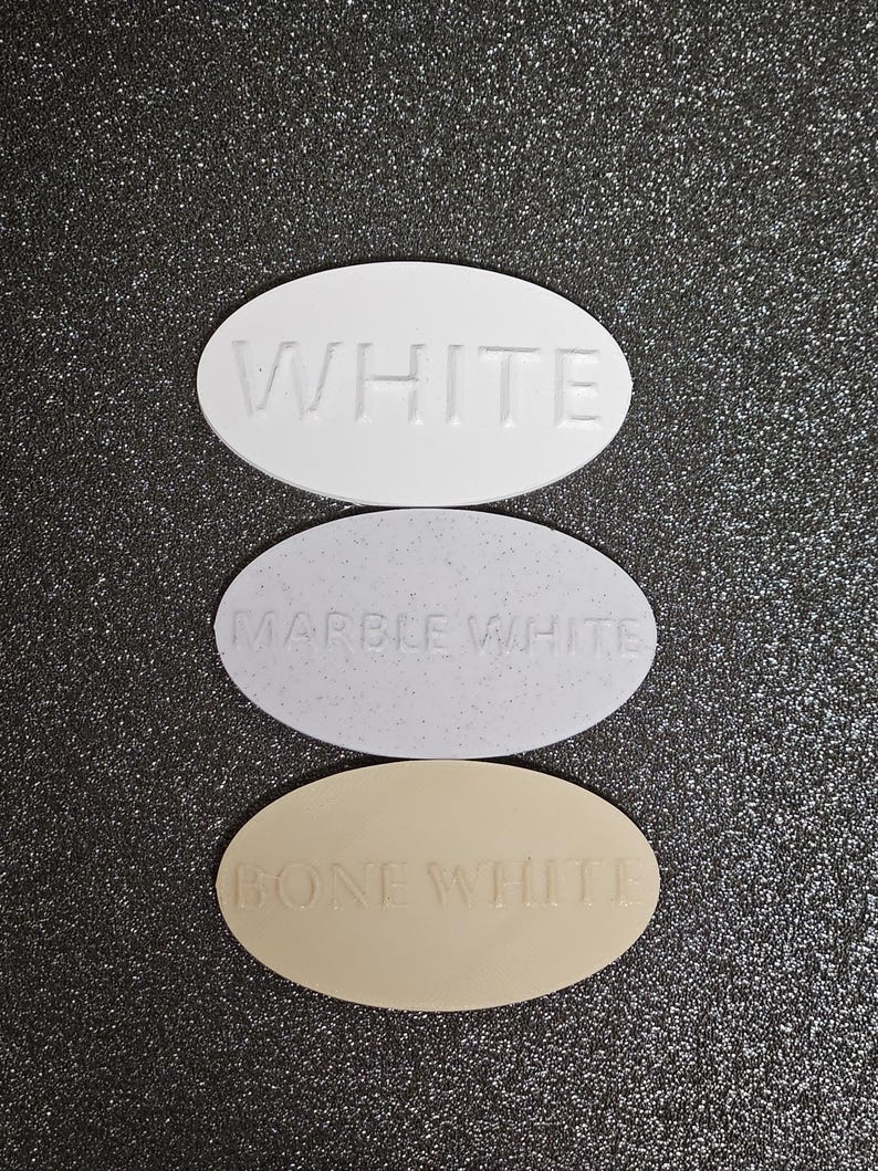 May include: Three oval-shaped paint chips, each with a different shade of white. The top chip is labelled "WHITE", the middle chip is labelled "MARBLE WHITE", and the bottom chip is labelled "BONE WHITE".