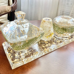 Könnte beinhalten: Ein Set aus drei durchsichtigen Harzbehältern mit Blattgoldakzenten und getrockneten Farn- und Blumenakzenten. Die Behälter befinden sich auf einem durchsichtigen Harztablett mit Blattgoldakzenten.
