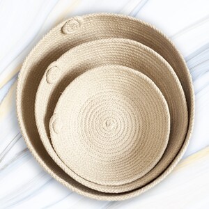 May include: Three natural woven rope baskets, nested together, with a light beige color. The baskets are made of thick rope and have a circular shape.